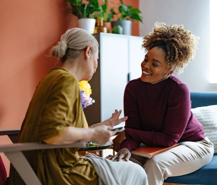 Caregiver smiling while talking with an elderly woman during a supportive home visit