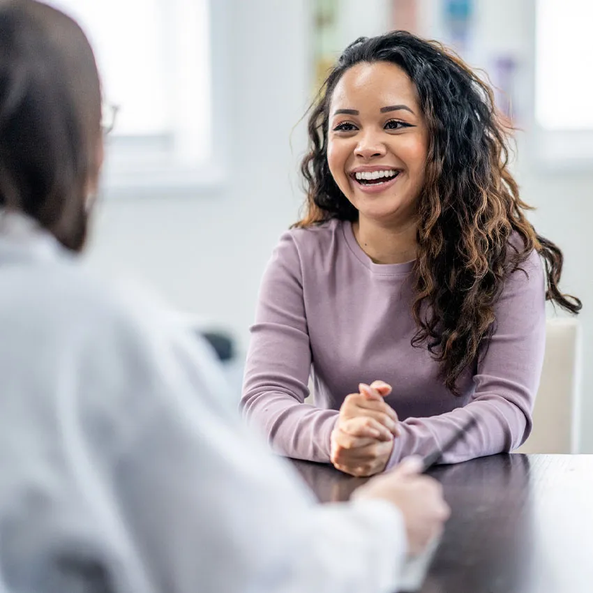 Smiling woman with curly hair in mauve top engaged in friendly conversation across a table during a meeting