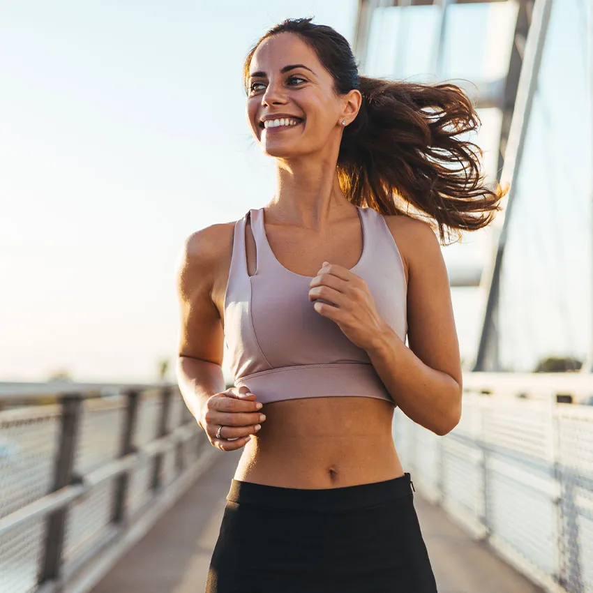 Smiling fit woman running on bridge during sunrise, outdoor fitness workout and cardio training