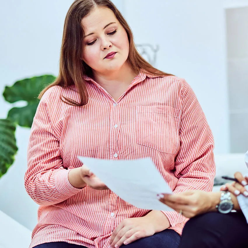 Woman in pink striped shirt reviewing paperwork during an office consultation with a professional