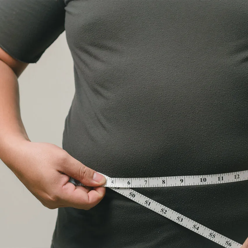 Person in dark shirt measuring waist with tape measure, close-up showing midsection and hands