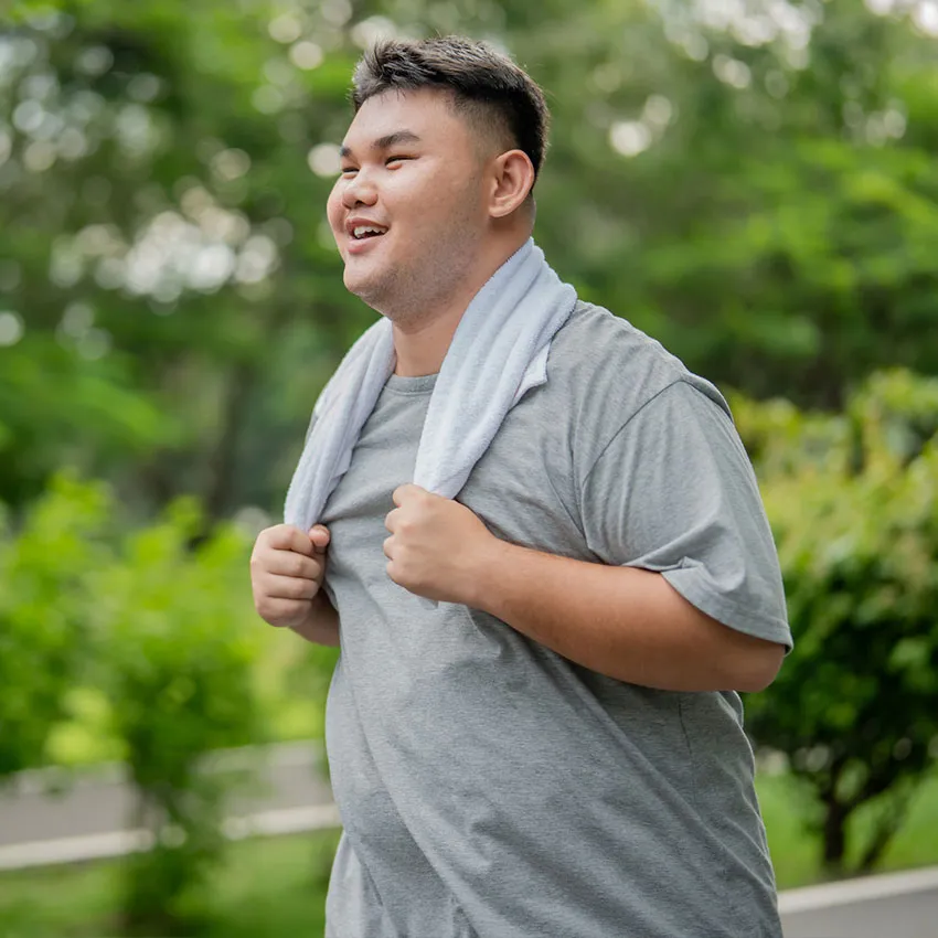 Smiling man with towel around his neck walking outdoors in a gray t-shirt during a park fitness walk