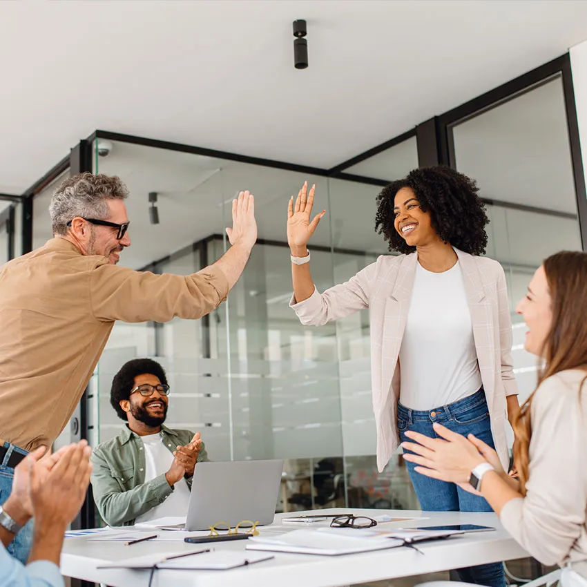 Diverse office team celebrating success with high-five during collaborative business meeting