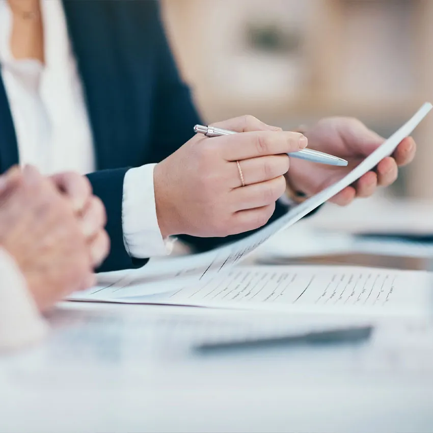 Person in business attire pointing with a pen at documents, reviewing contract pages during meeting