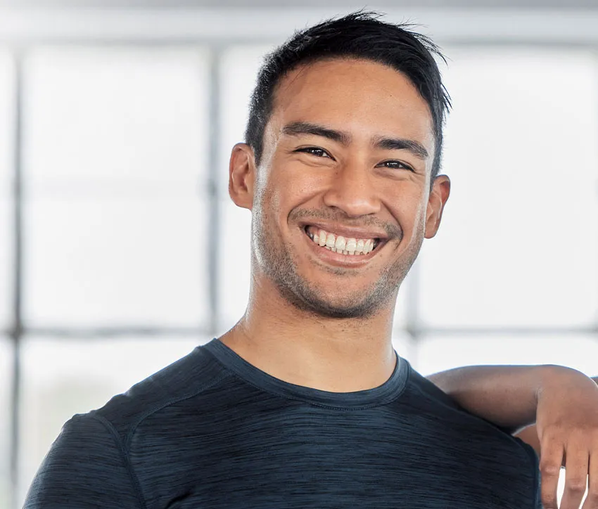 Smiling athletic man in dark workout shirt, close-up portrait with bright indoor gym windows in background