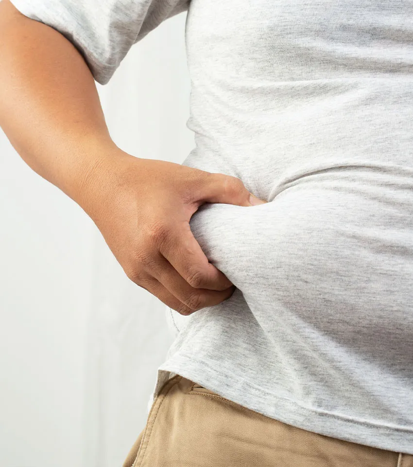 Close-up of a person pinching belly fat through a gray T-shirt above khaki pants