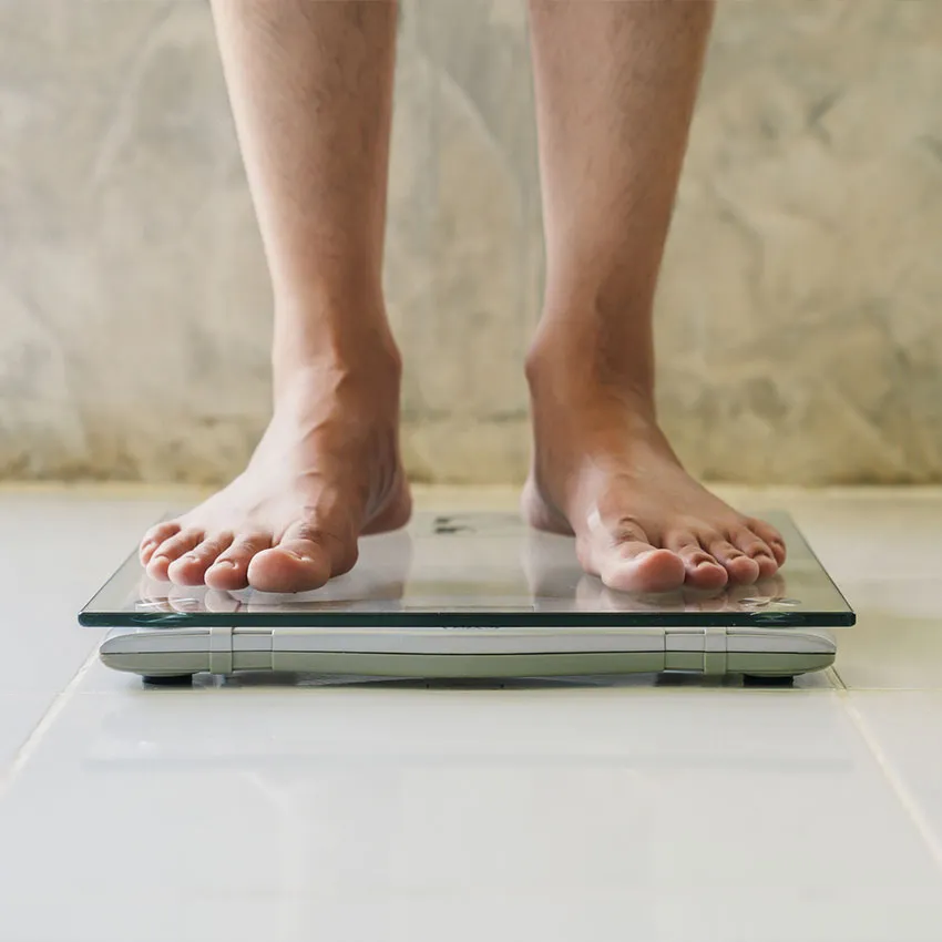Person's bare feet on a glass digital bathroom scale on white tile, measuring body weight