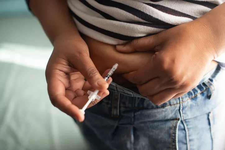 Person giving insulin injection into abdominal subcutaneous tissue with syringe, diabetes self-injection close-up